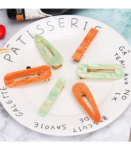 Detailed view of six acetate hair clips with marble textures on a white ceramic plate