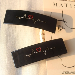 Détail de la barrette en acétate noir avec strass battement de cœur et motif cœur rouge