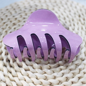 Dettaglio di una pinza per capelli in acrilico viola lucido su sfondo di paglia intrecciata