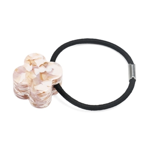 Macro detail of acetate four-leaf clover charm and high-elastic hair tie with metal clasp
