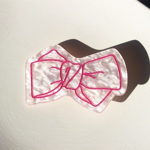Pince à cheveux noeud nacré avec des contours roses sur un fond texturé élégant