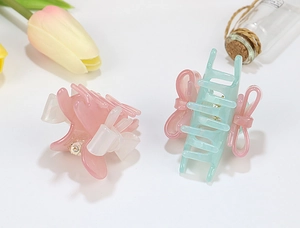 Close-up of mint green and pink acrylic bow hair claw clips with decorative floral accents
