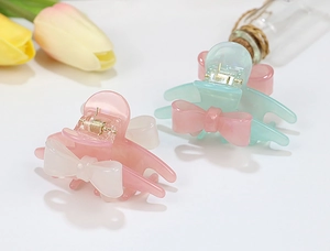 Detail of pastel acrylic hair claws in pink and green with marble texture and bow design