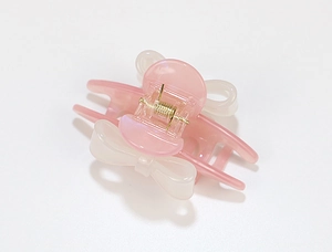 Detail of a pink and white acetate bow hair claw clip with golden metal spring