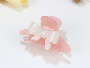 Macro detail of a translucent pink acrylic hair claw clip with a white bow ornament