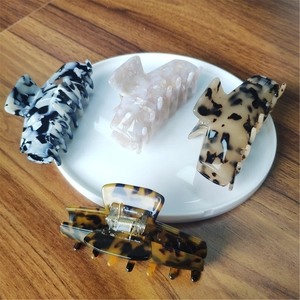 Macro view of four acetate hair claws in marble and tortoiseshell patterns with metal springs