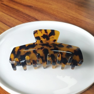 Detail of tortoiseshell patterned acetate hair claw clip on white ceramic plate