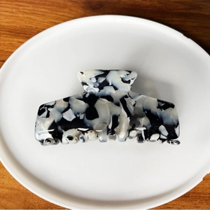 Close-up of a large black and white marble patterned acetate hair claw clip on a white tray