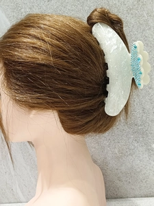 Detailed side view of a large white pearlized shark hair clip with blue rhinestones