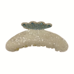Detail view of cream white acetate hair claw clip with peacock blue rhinestone accents