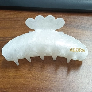 Detailed close-up of white marble pattern hair claw clip with golden ADORN lettering