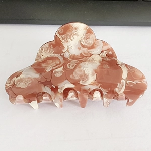 Detail view of the marbled red-brown and cream acetate claw clip with arc tooth comb