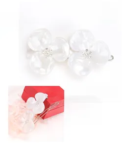 Detailed macro view of dual white acetate flower petals and rhinestone center hair clip