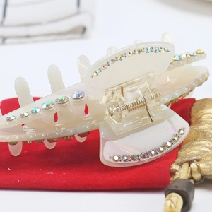 Detail view of large cream acetate hair claw clip with colorful rhinestones on red velvet