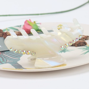 Close-up of pearl white acetate hair claw clip with colorful rhinestones on a decorative plate