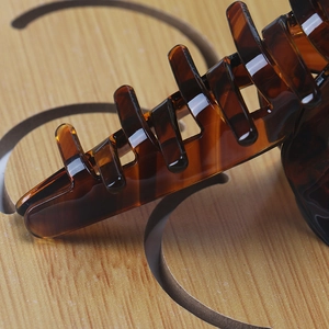 Detailed view of large dark amber acetate hair claw clip with tortoise shell pattern on wood
