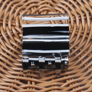 Détail d'une pince à cheveux carrée en acrylique à rayures noires et blanches sur plateau