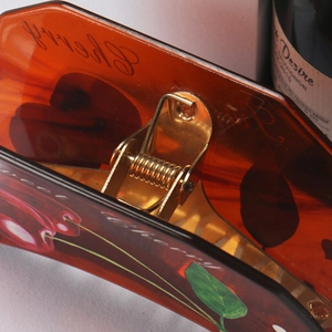 Close-up of translucent amber acetate claw clip with cherry pattern and Sweet text