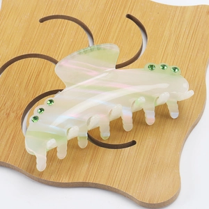 Large light green acetate hair claw clip with colorful rhinestones on a wooden stand