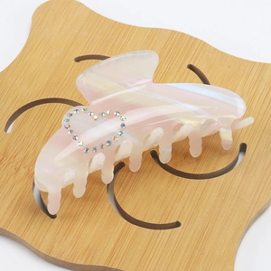 Detail of a pearlescent heart hair claw clip with colorful rhinestones on wood background