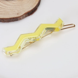 Detail of yellow wavy acetate hair clip with golden metal base on white background