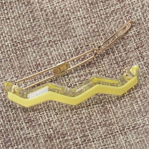 Close-up of a lemon yellow wavy acetate hair clip with a polished gold metal base