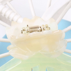 Gros plan sur la pince à cheveux lotus en acétate avec pétales crème et dents vertes