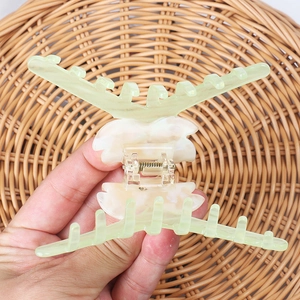 Détail de la grande pince à cheveux en acétate vert clair sur un support en rotin tissé