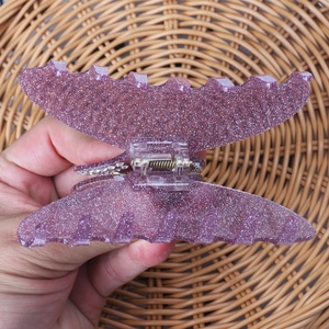Détail d'une pince à cheveux papillon violette scintillante avec ressort en métal sur osier