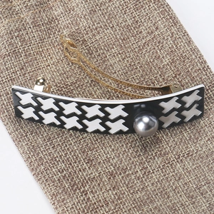 Detail view of houndstooth pattern hair clip with a grey pearl on golden metal base