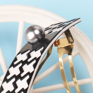 Detail of houndstooth hair clip with a grey pearl on a gold metal spring base