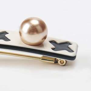 Detail of houndstooth hair clip with cream acrylic base, black X pattern and large pearl