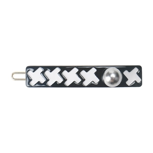 Detail of a black lacquered hair clip featuring white X patterns and a silver stud accent