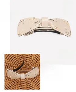 Detailed close-up of a beige acetate bow hair clip with sparkling rhinestone embellishments