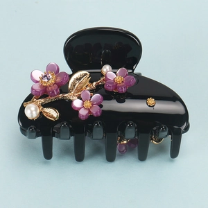 Detail of elegant black acetate claw clip with purple cat-eye flowers and pearls