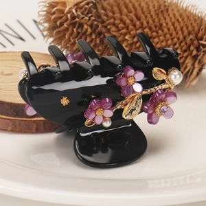 Detail of floral hair claw clip with purple petals and pearls on a white ceramic plate