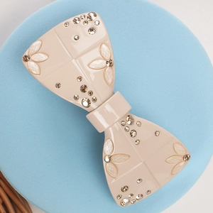 Close-up of beige acetate bow hair clip with champagne rhinestones and pearly leaves