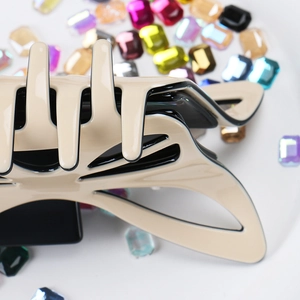 Detail of a large bow hair claw with beige finish and black outlines on a crystal background