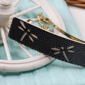 Macro shot of black acetate spring hair clip with white dragonfly pattern detail