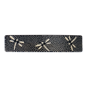 Detail view of a vintage barrette with black honeycomb pattern and white dragonflies