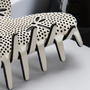 Detail of cream acetate hair claw with black trim and elegant hollowed-out patterns