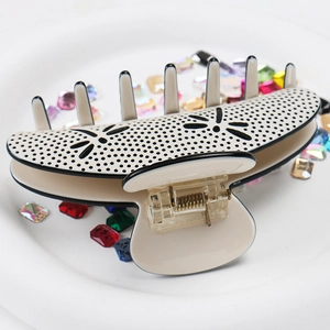 Detail view of a beige matte hair claw clip with black polka dots and floral cutouts