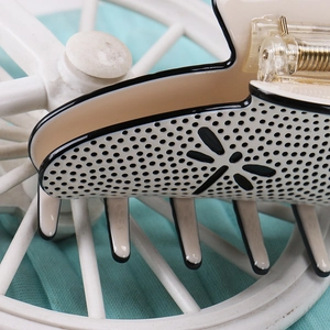 Close-up of beige acetate hair claw clip featuring black borders and dragonfly cutouts