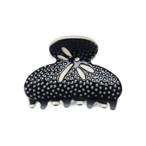 Detailed view of black acetate hair claw with white polka dots and floral pattern texture