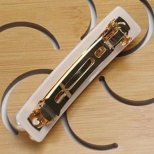 Détail d'une pince à cheveux beige de 8cm avec boucle dorée et décorations en perles