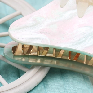 Detail of pink and green marbled acrylic hair claw with golden metal teeth structure