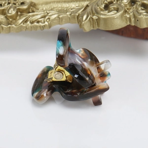 Close-up of tortoise shell mini hair claw clip with gold metal spring on white surface