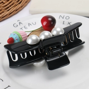 Detail of a premium black acetate shark hair claw clip with large pearls on a white plate