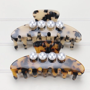 Detail view of two acetate hair claws with tortoiseshell patterns and white pearls