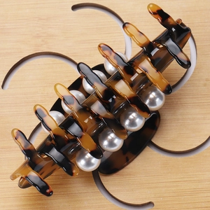 Macro detail of tortoiseshell acetate hair claw clip with elegant white pearls on wood